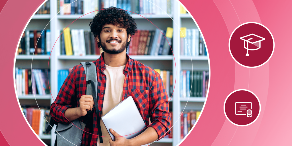A male international student stands holding his backpack and laptop in a well-lit space with lots of books (a library or office).