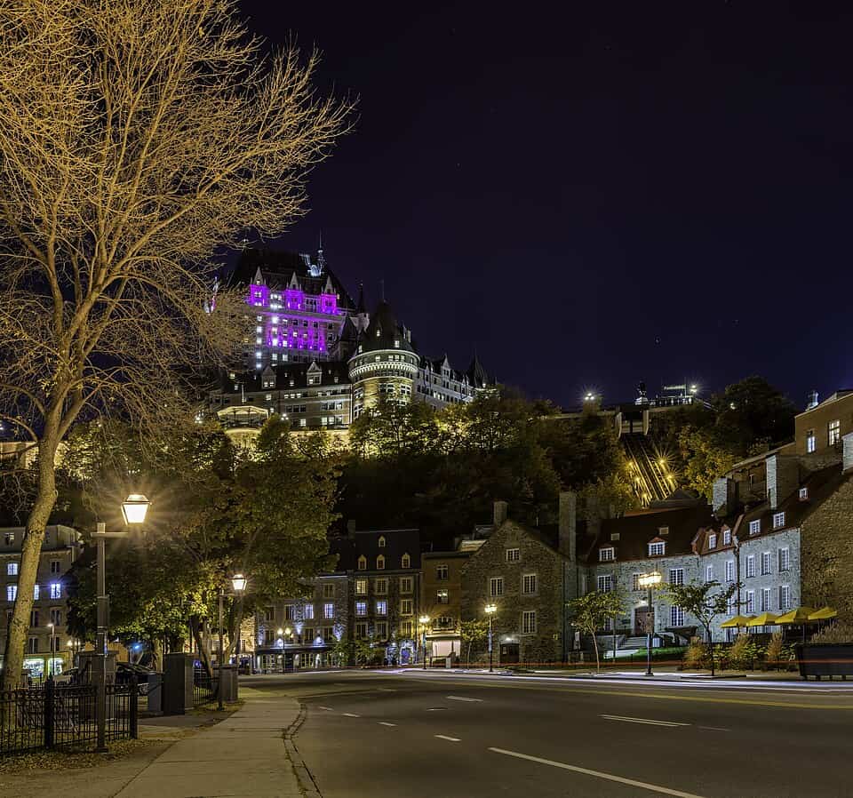 A view of Old Quebec within Quebec City at night - buildings climb a tall hill, topped by the Fairmont lit in magenta light.