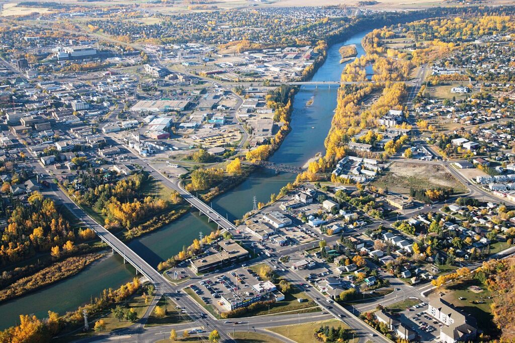An aerial view of the city of Red Deer, Alberta, in the fall: a river bisects the city, with bridges crossing it. The downtown is on the left side, and more residential areas are on the right. The trees (largely aspen birch) have turned yellow for the fall.