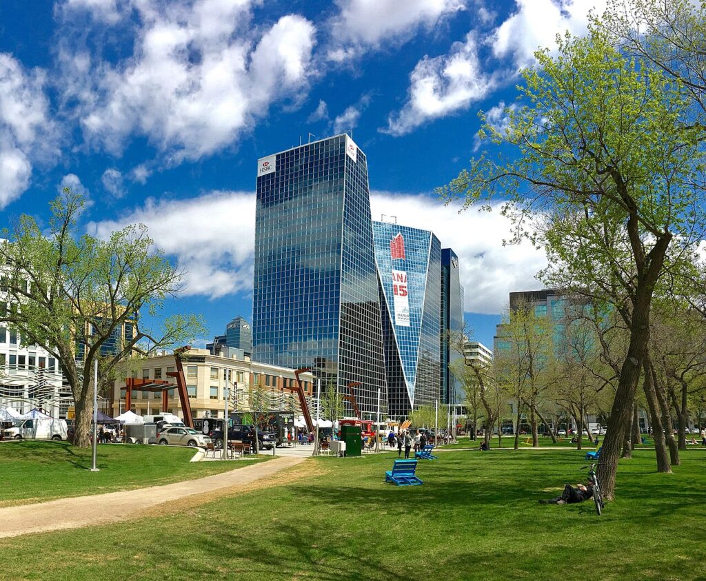 Tall downtown towers with blue glass exteriors, framed by a city park in Regina, Saskatchewan.