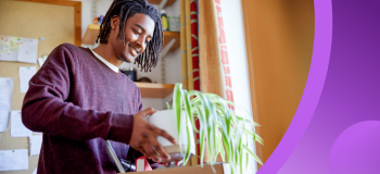 A Black international student holds a potted plant as he moves into his dorm room.