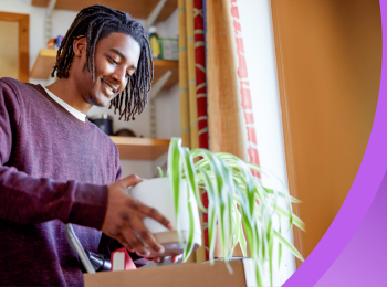 A Black international student holds a potted plant as he moves into his dorm room.
