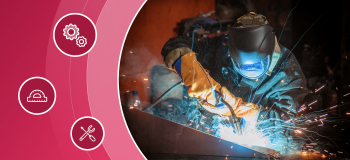 A welder in full gear (flame-resistant helmet, gloves, and coat) works with tools.