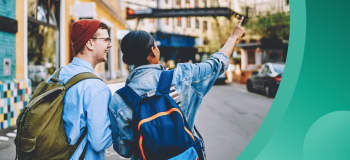 Two students walk along an urban street, wearing backpacks and fall clothing